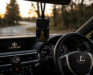 A black car air freshener hanging from the rearview mirror inside a Lexus car, with the product label reading 'SILENT SIN'.