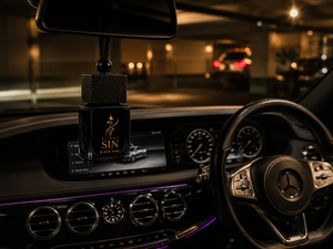 A Mercedes-Benz car interior at night with a black hanging car air freshener ornament featuring a gold 'Silent SIN' logo, suspended in front of the windshield. Silent Sin Automotive Elixir Car Fragrance
