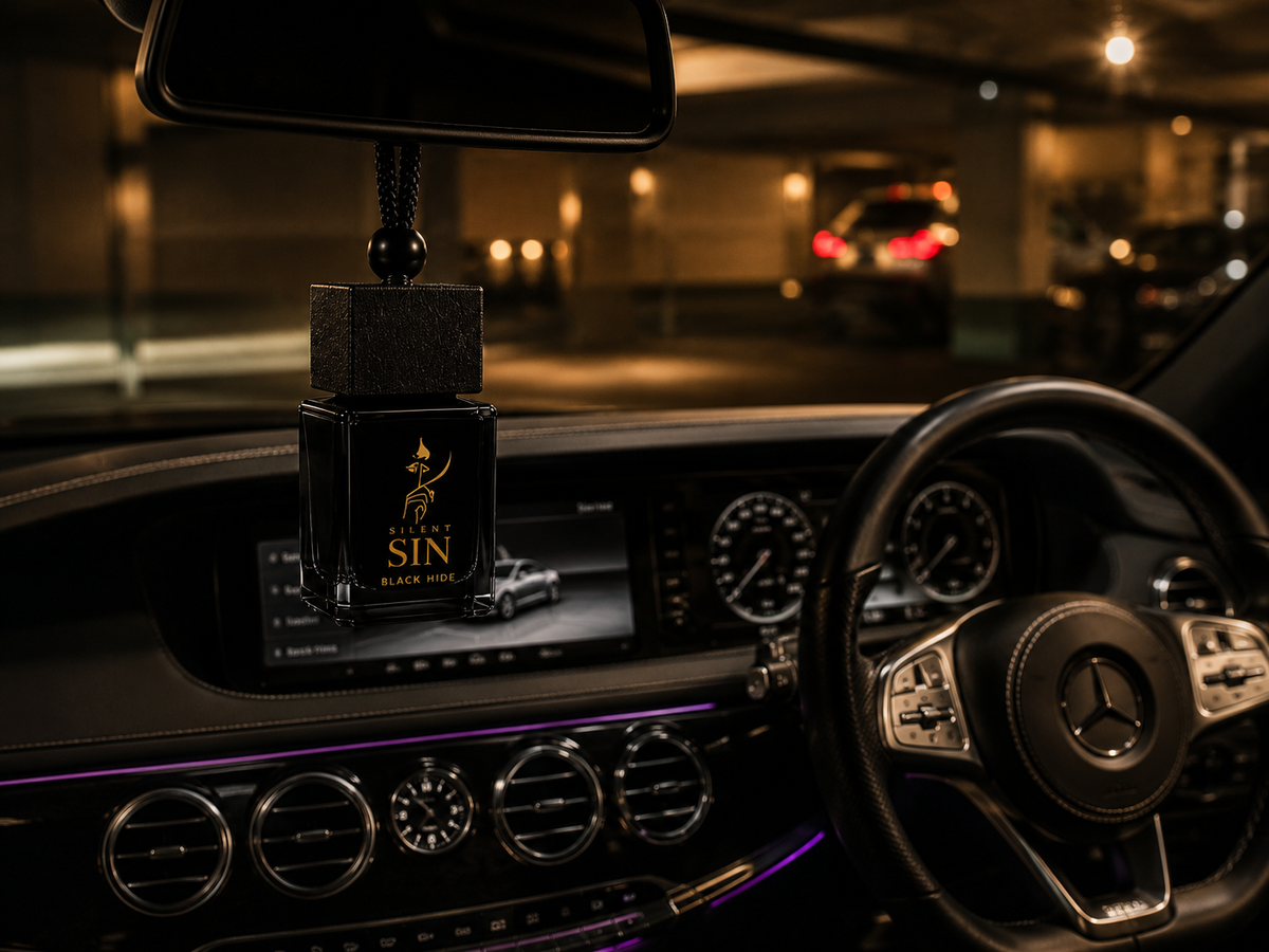 A Mercedes-Benz car interior at night with a black hanging car air freshener ornament featuring a gold 'Silent SIN' logo, suspended in front of the windshield. Silent Sin Automotive Elixir Car Fragrance