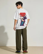 A model from the back wearing a white graphic t-shirt with a large red and purple 'AURA TOUR 2026' print, paired with olive green trousers and brown shoes, set against a minimalist beige studio background. 