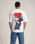A man viewed from behind wearing a white t-shirt with a large graphic print on the back featuring the text 'AURA TOUR' in red and a purple-haired performer, paired with blue jeans, against a plain beige background.