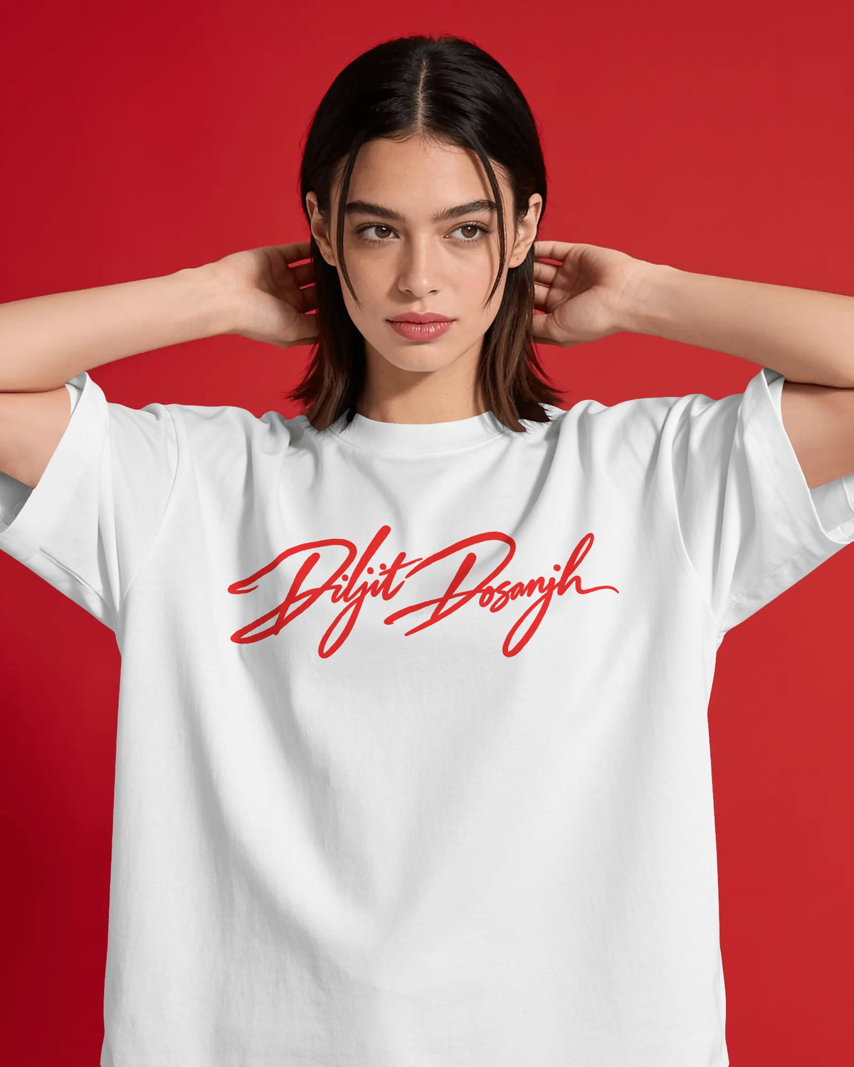 A woman wearing a white short-sleeve T-shirt with a red cursive script graphic across the chest, posed against a solid red background. Diljit Dosanjh Aura Tour India Tshirt.