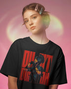 A young woman with her hair in a half-up bun wearing a black graphic t-shirt. The shirt features a large red and black graphic print of a character holding a camera, with the text 'Diljit Dosanjh in bold red letters.
