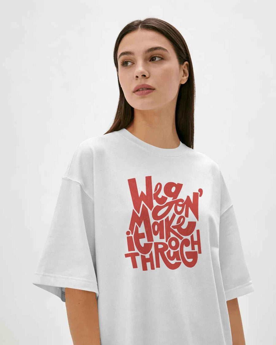 A woman wearing an oversized white t-shirt with a red graphic text print that reads 'We're Making It Through' on the front, set against a plain light gray background. Fred Again India Concert collection