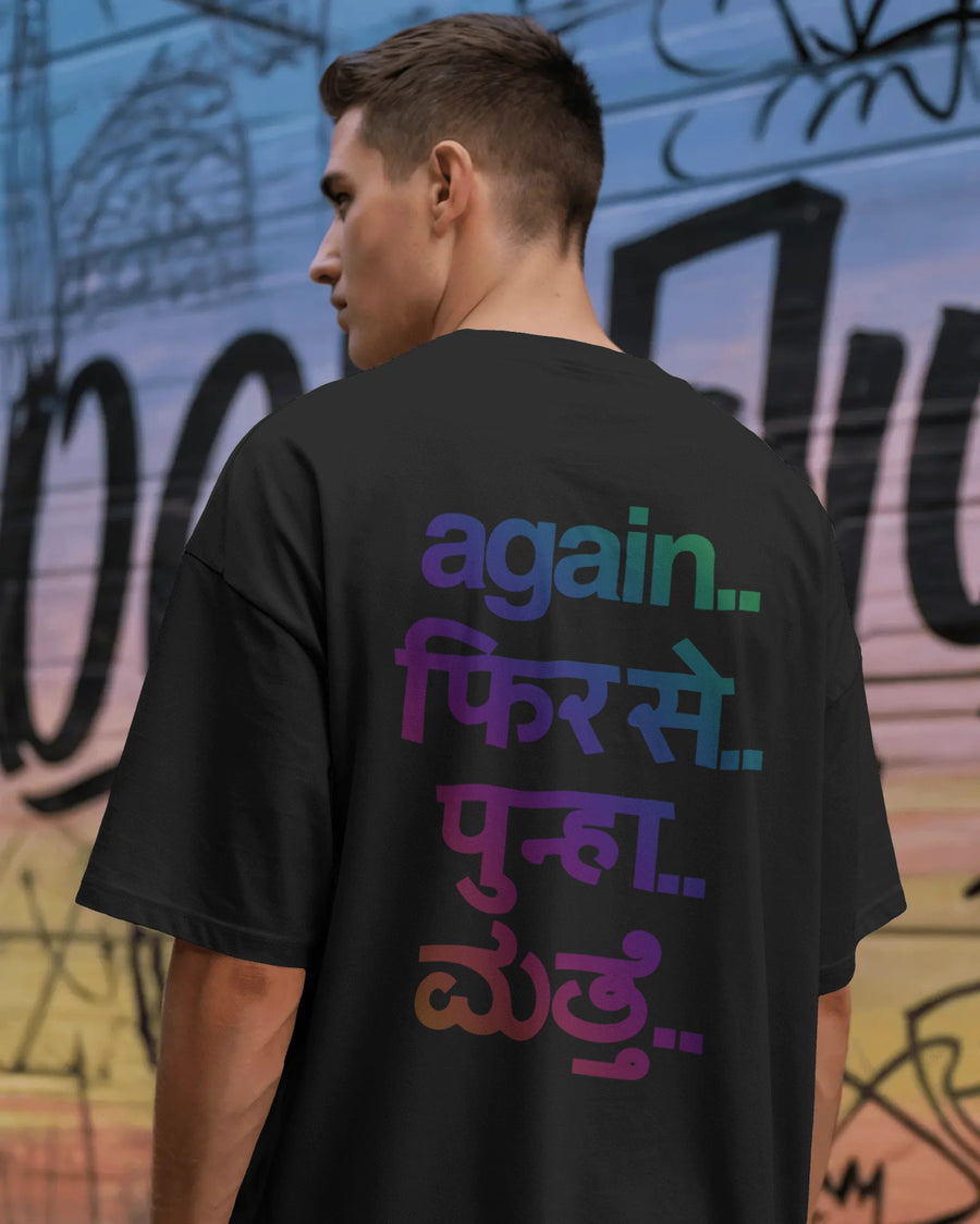 A man viewed from behind wearing a black t-shirt with colorful gradient Hindi text printed on the back. The background is a graffiti-covered wall. Nitorious Atelier Fred Again.. concert collection