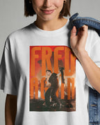 A woman wearing a white graphic t-shirt with a large orange and red 'FRED AGAIN' print on the front, holding a denim jacket over her shoulder against a neutral gray background.
