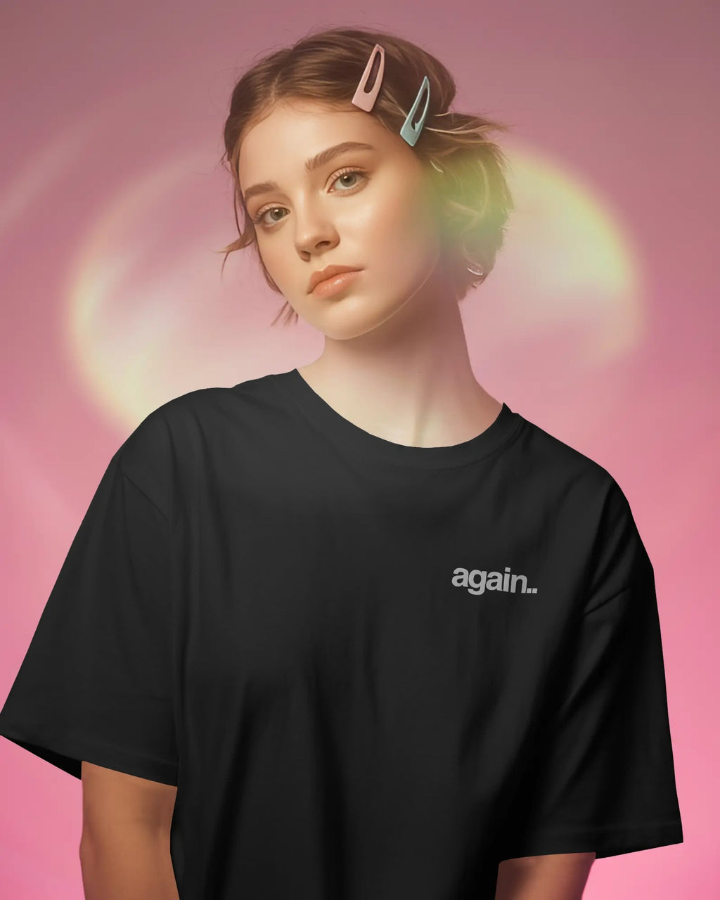 A woman wearing an oversized black t-shirt with the word 'again.' printed in white on the left chest, posed against a pink background with a soft green glow.