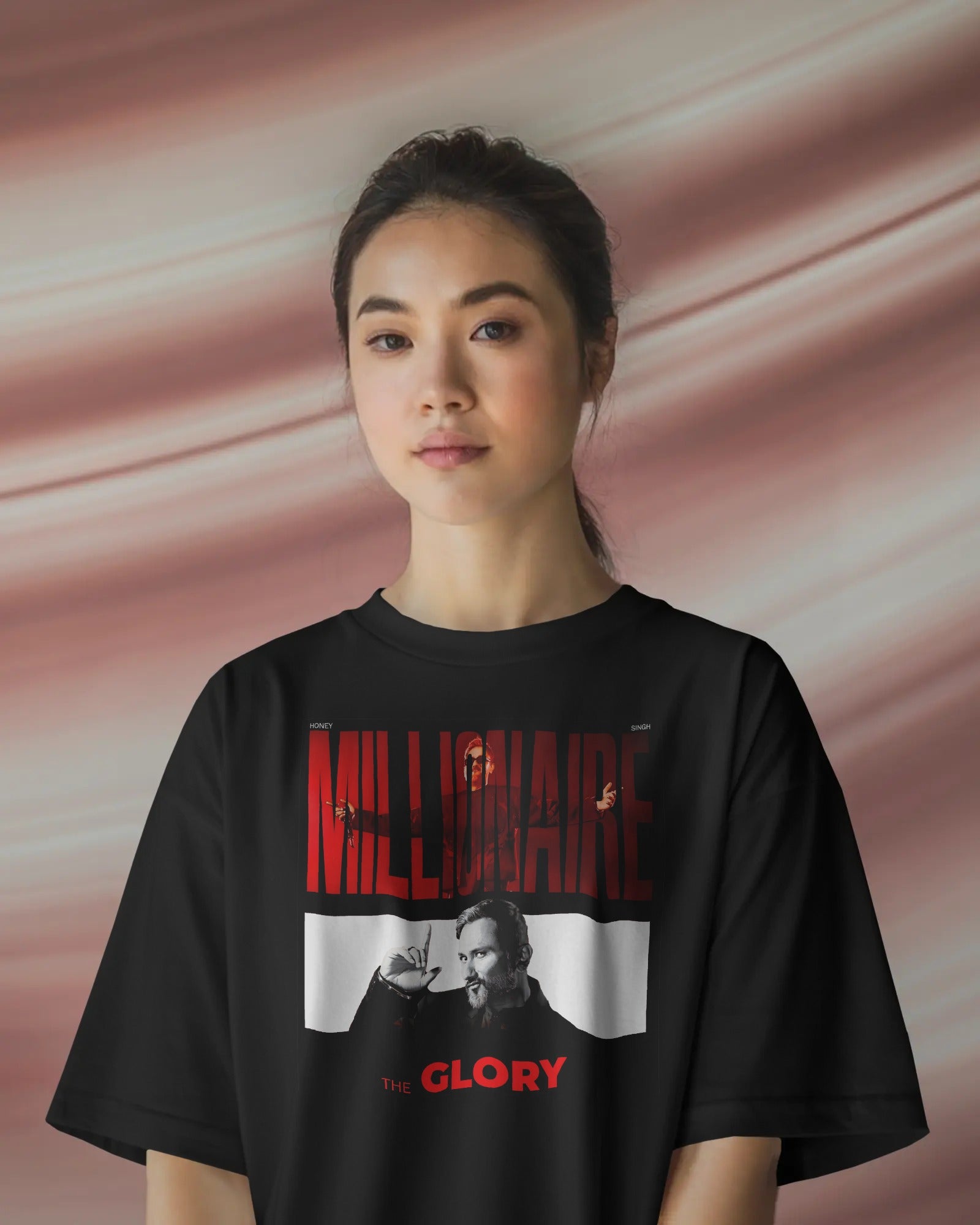 Person wearing a black t-shirt with 'Millionaire' and 'The Glory' graphic design on a pink background