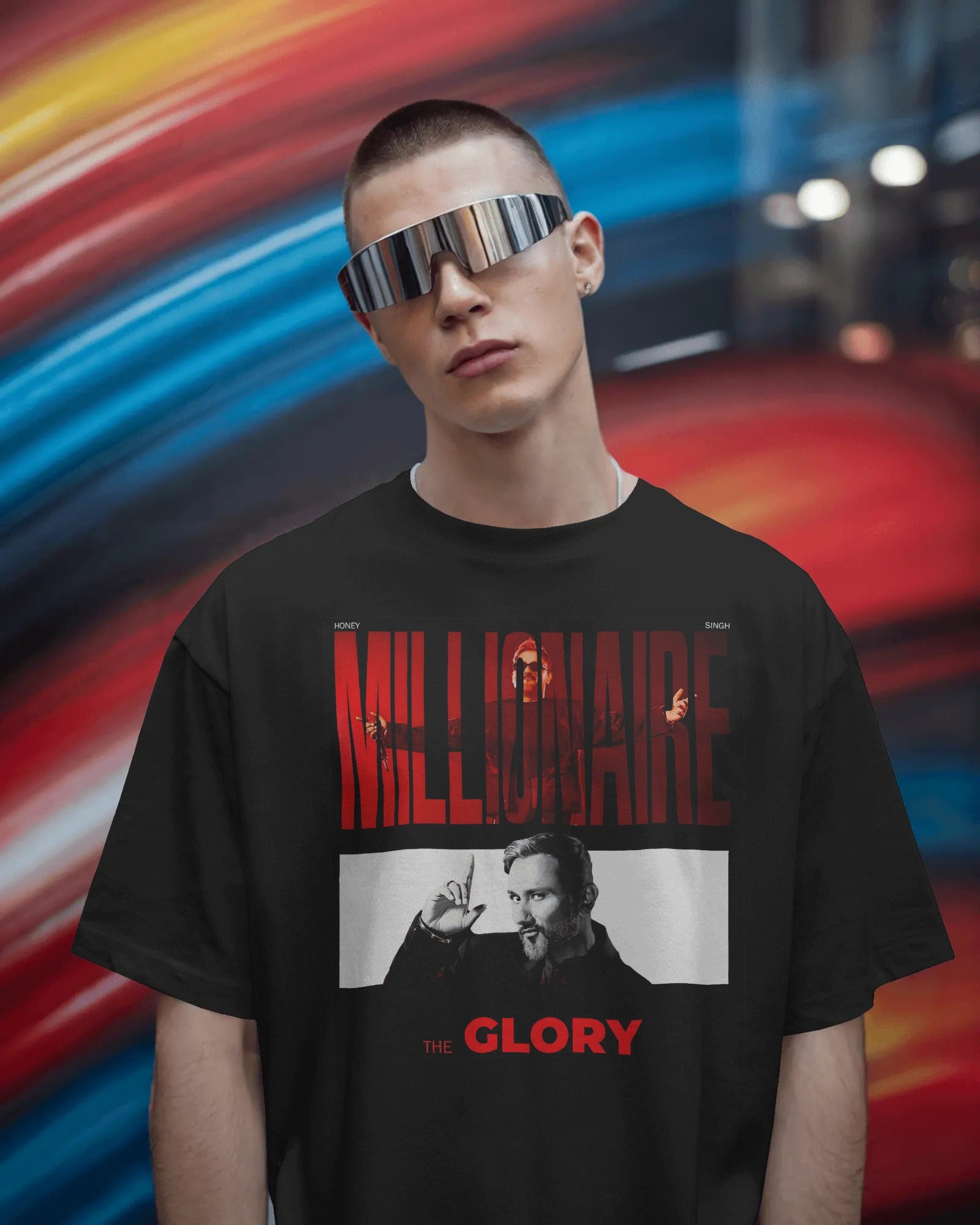 Person wearing a black t-shirt with 'Millionaire' and 'The Glory' graphic design against a colorful blurred background.