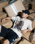 Man sitting among cardboard boxes wearing a white t-shirt with a graphic design of Kanye West from Nitorious Atelier 