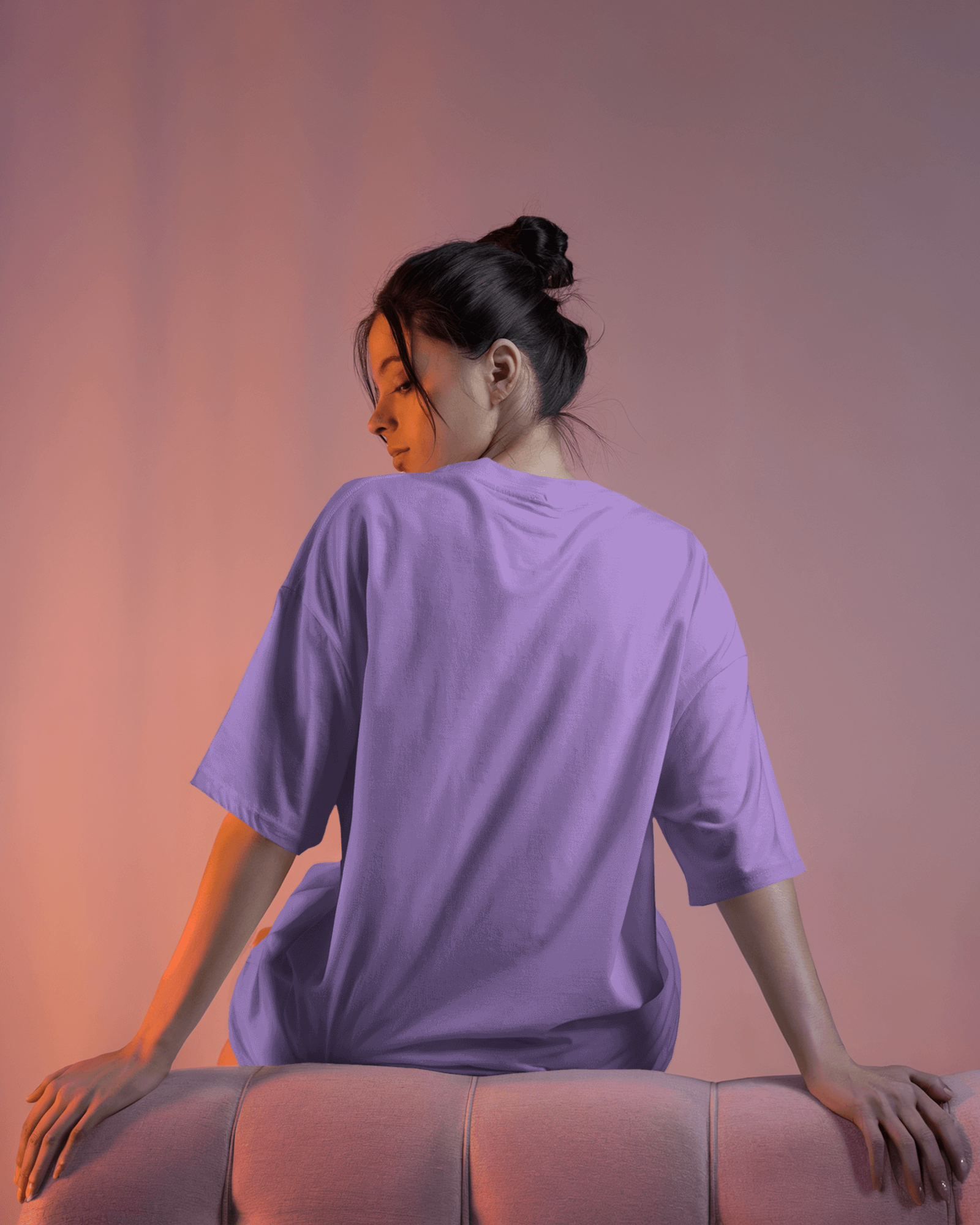Woman wearing a lavender Labubu oversized t-shirt sitting on a pink couch against a pink background