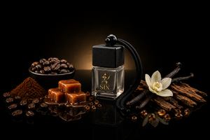 A clear glass perfume bottle with a black cap and black cord, labeled Silent SIN by Nitorious Atelier, styled with coffee beans, caramel cubes, vanilla beans, and a vanilla flower on a black reflective background. Silent Sin Automotive Elixir Car Fragrance