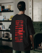 Person wearing a black t-shirt with red 'Batman' logo on the back in an indoor setting.