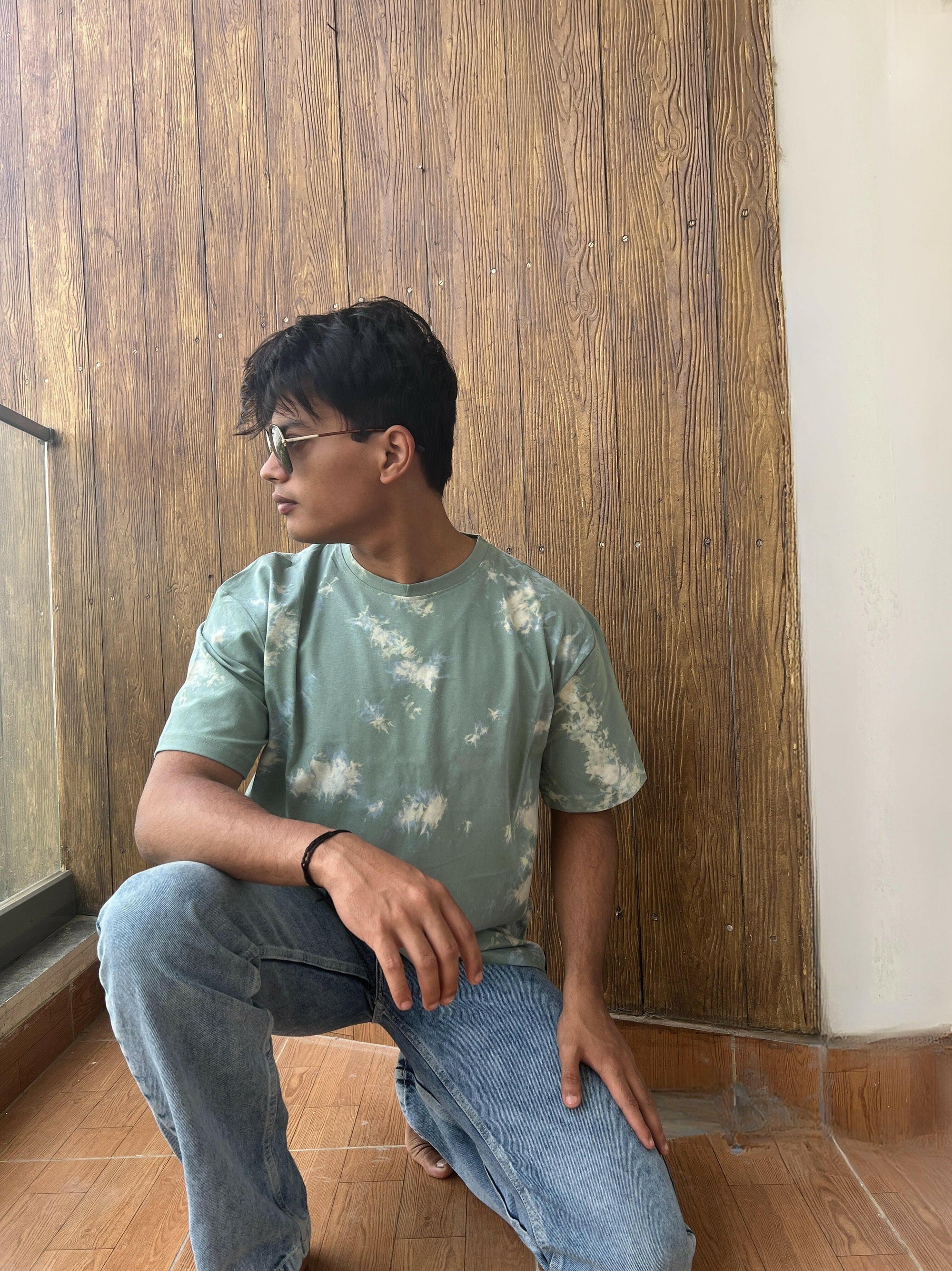 A close-up shot of a Nitorious Atelier Tie and Dye Sea Green 100% Cotton fabric Unisex Oversized T-shirt. The fabric displays a rich dark blue hue with intricate tie and dye patterns, meticulously crafted with high-quality cotton material