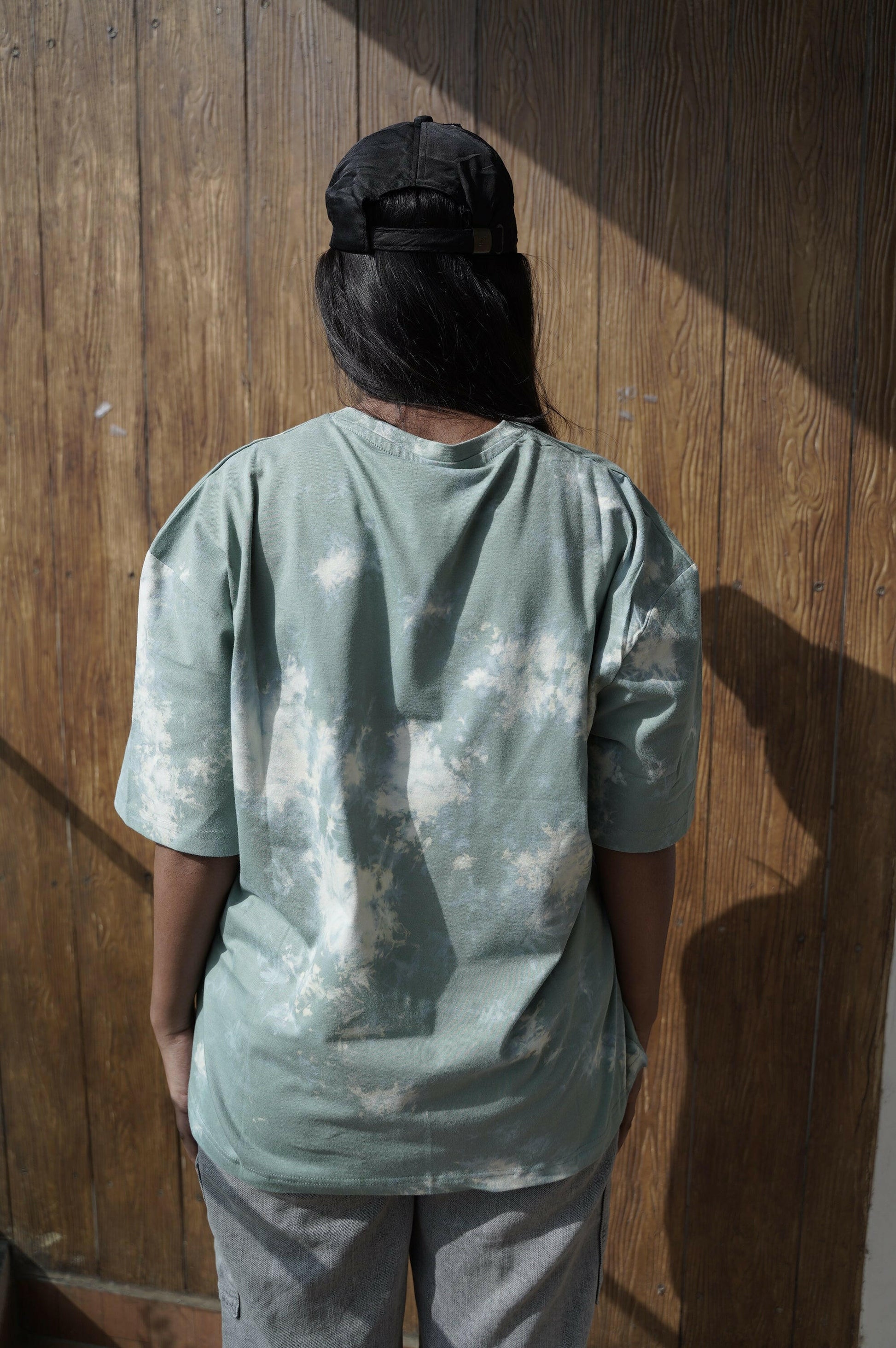 A close-up shot of a Nitorious Atelier Tie and Dye Sea Green 100% Cotton fabric Unisex Oversized T-shirt. The fabric displays a rich dark blue hue with intricate tie and dye patterns, meticulously crafted with high-quality cotton material