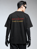 Person wearing a black t-shirt with text on the back, standing against a gray background