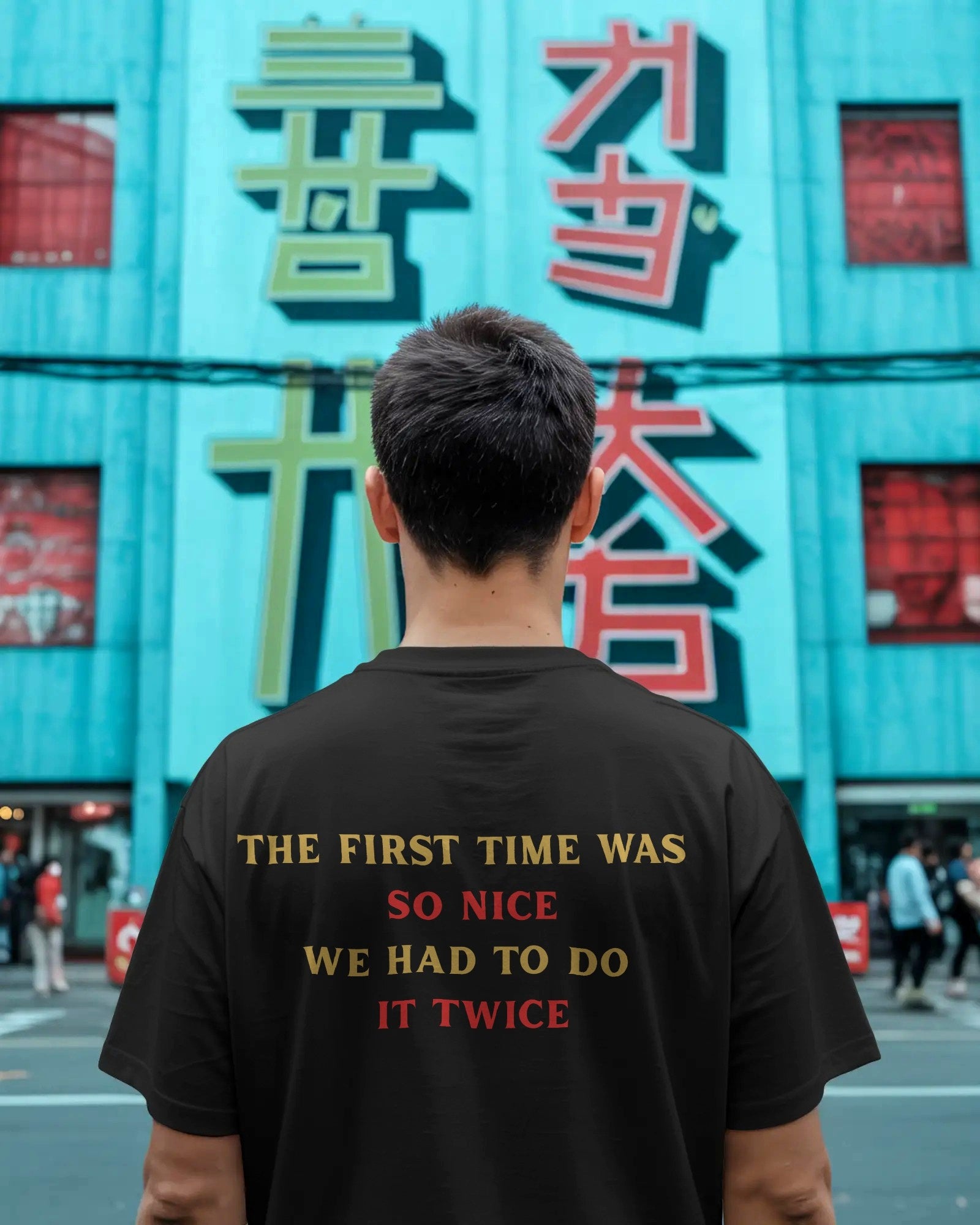 Person wearing a black t-shirt with text in front of a colorful building with large characters. Nitorious Atelier RCB Champions 2026 Tshirt from Puma
