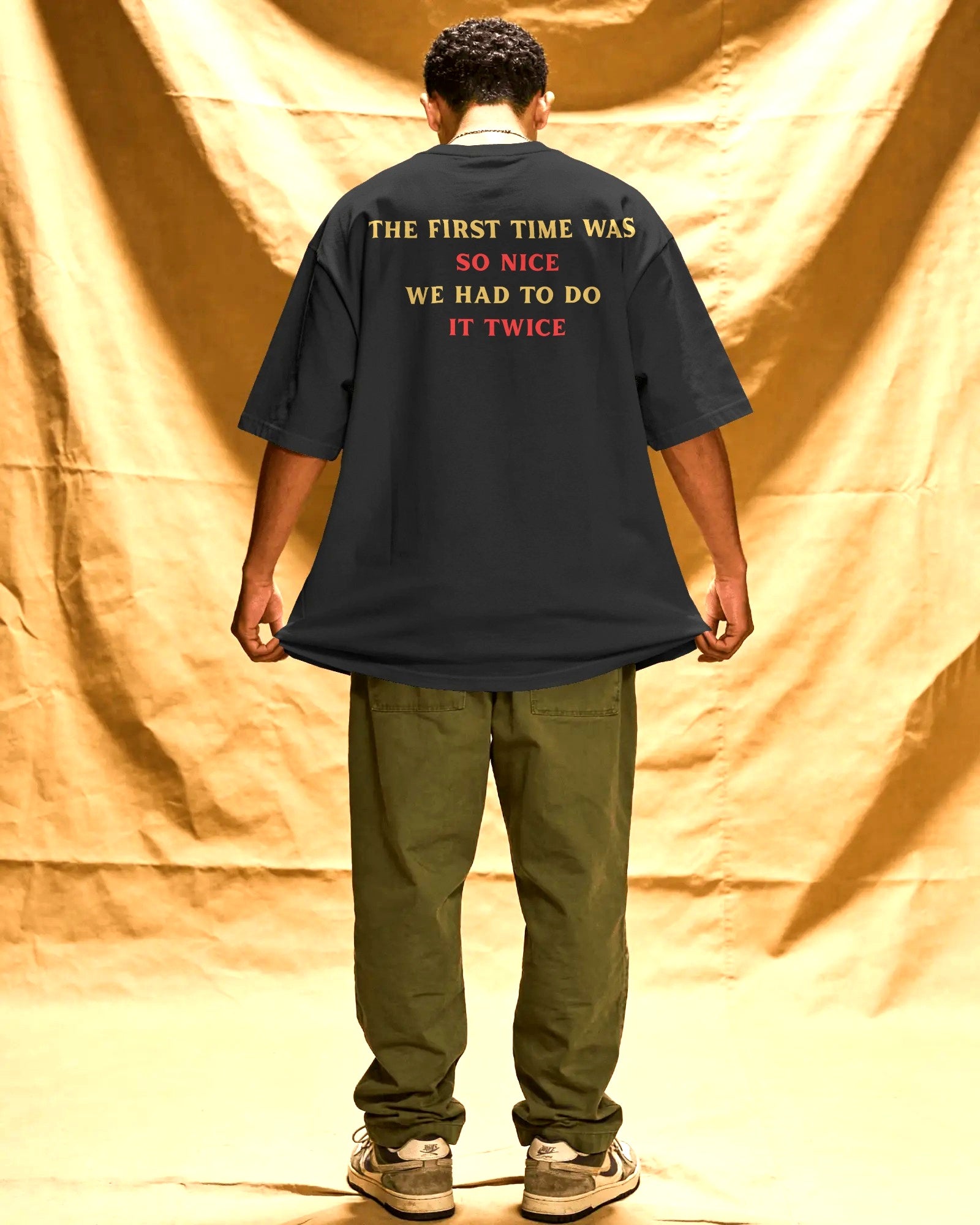 Person wearing a black t-shirt with text on the back, standing against a gold curtain.  Nitorious Atelier RCB Champions 2026 Tshirt from Puma