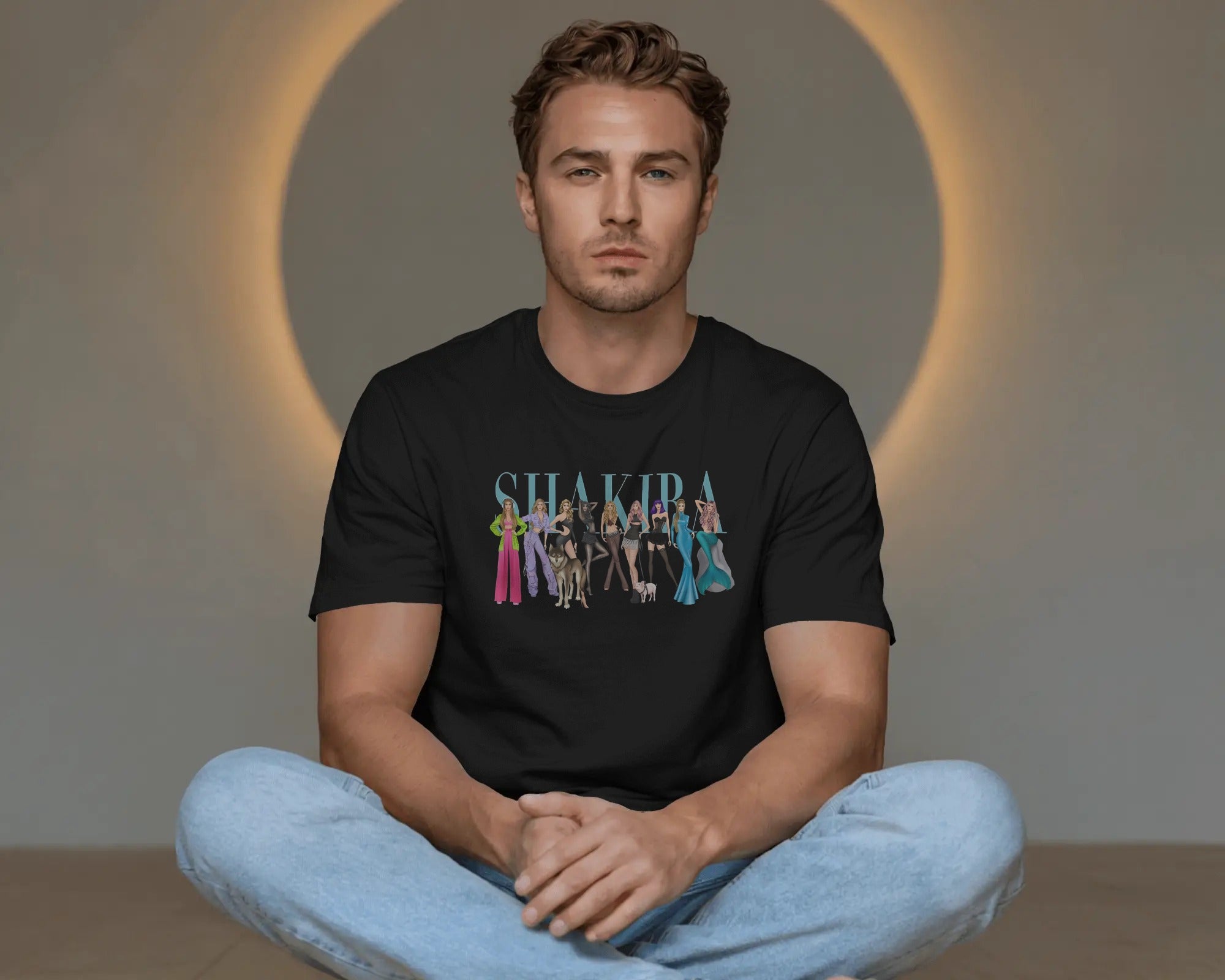 Man wearing a black t-shirt with 'Shakira' graphic design sitting on the floor.