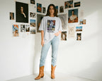 Woman wearing a 'Shakira' t-shirt in a room with artistic posters on the wall.