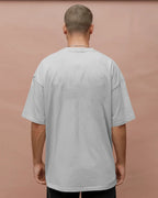Man wearing a light gray t-shirt against a pinkish-brown background