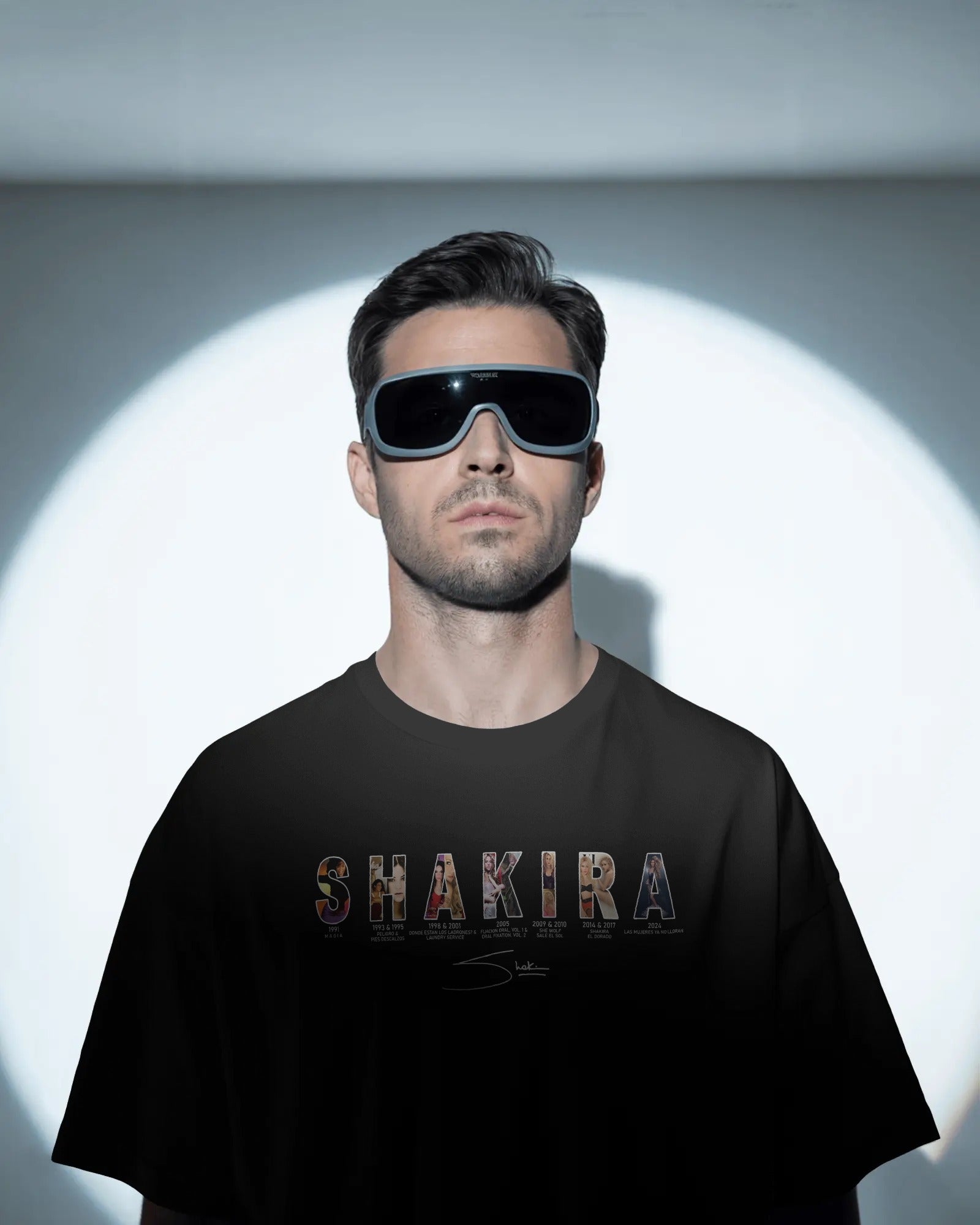 Man wearing sunglasses and a black t-shirt with 'SHAKIRA' printed on it, standing against a white background.