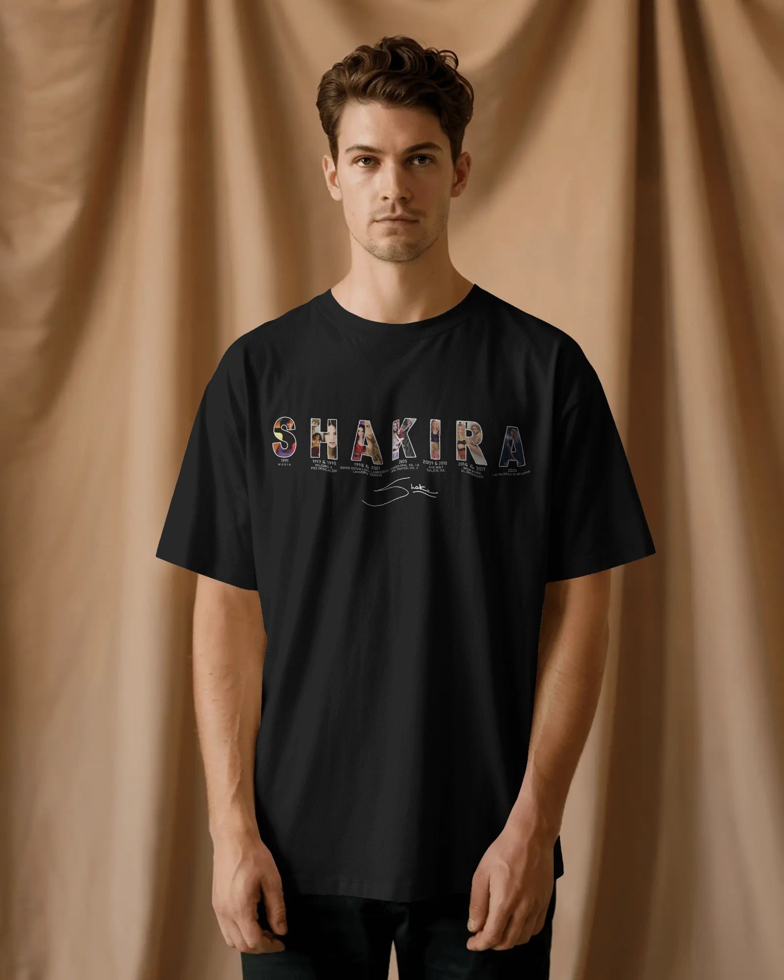 Person wearing a black t-shirt with 'SHAKIRA' printed on it against a beige curtain background