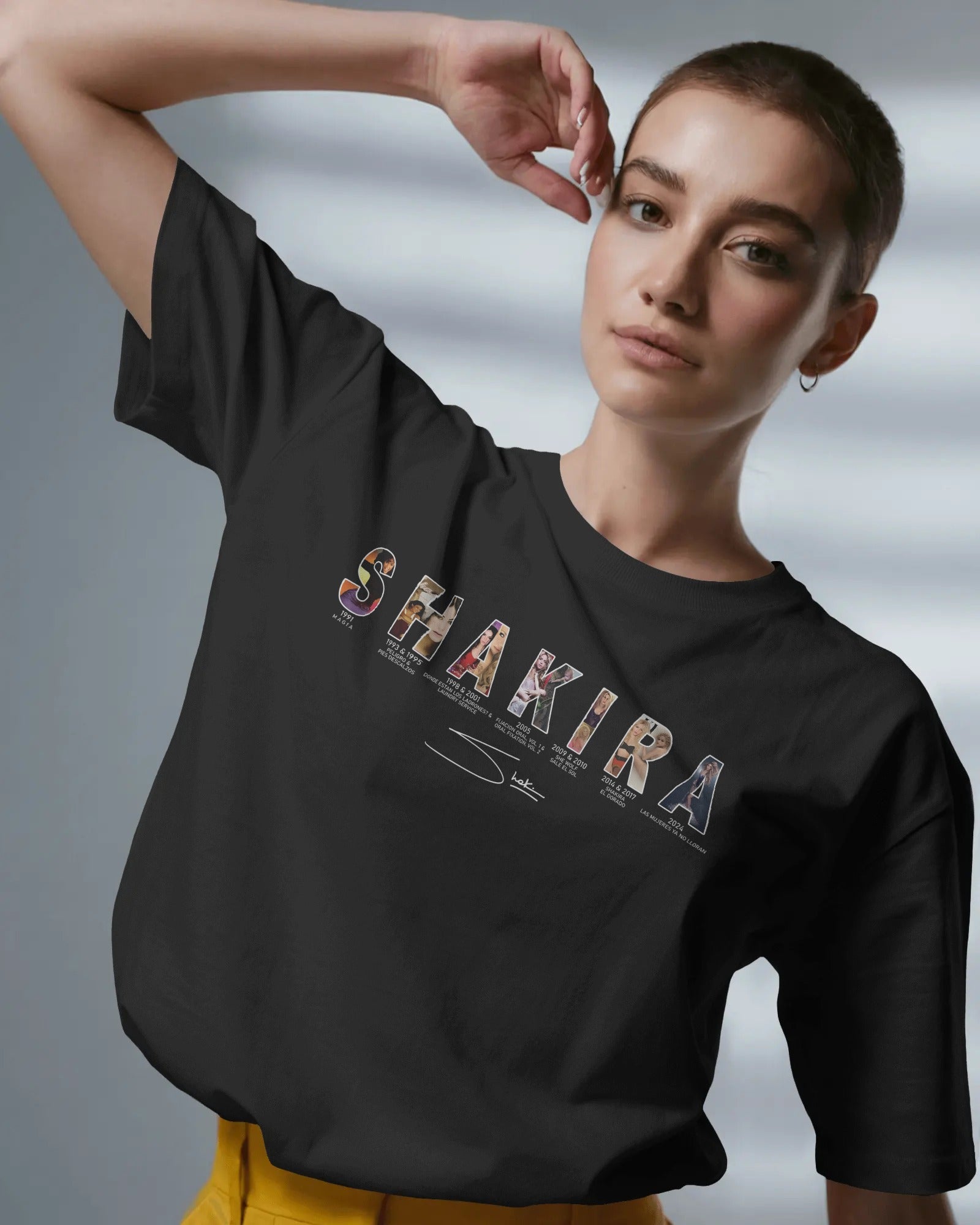 Person wearing a black t-shirt with 'Shakira' design on a gray background