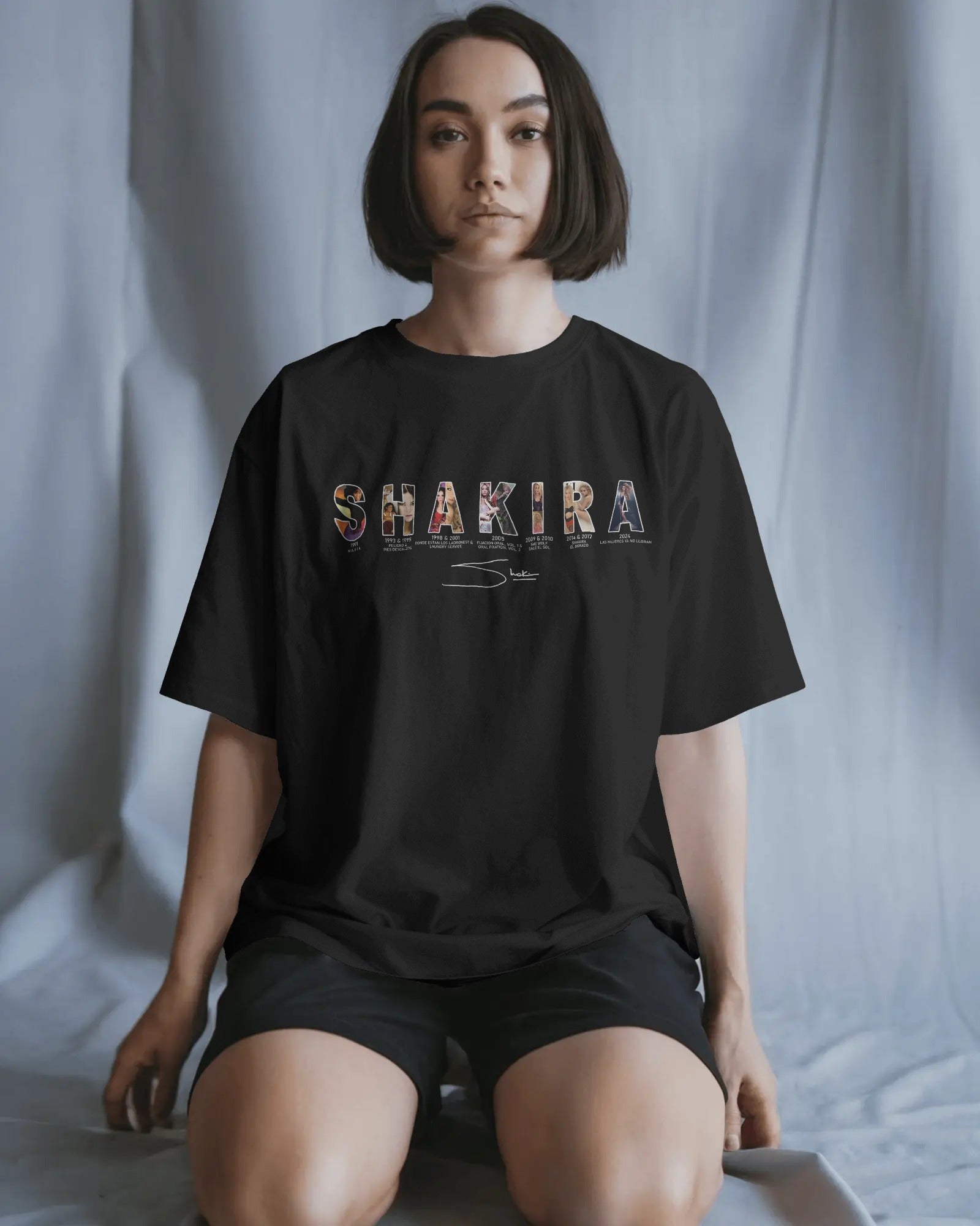 Person wearing a black t-shirt with 'SHAKIRA' printed on it against a plain background