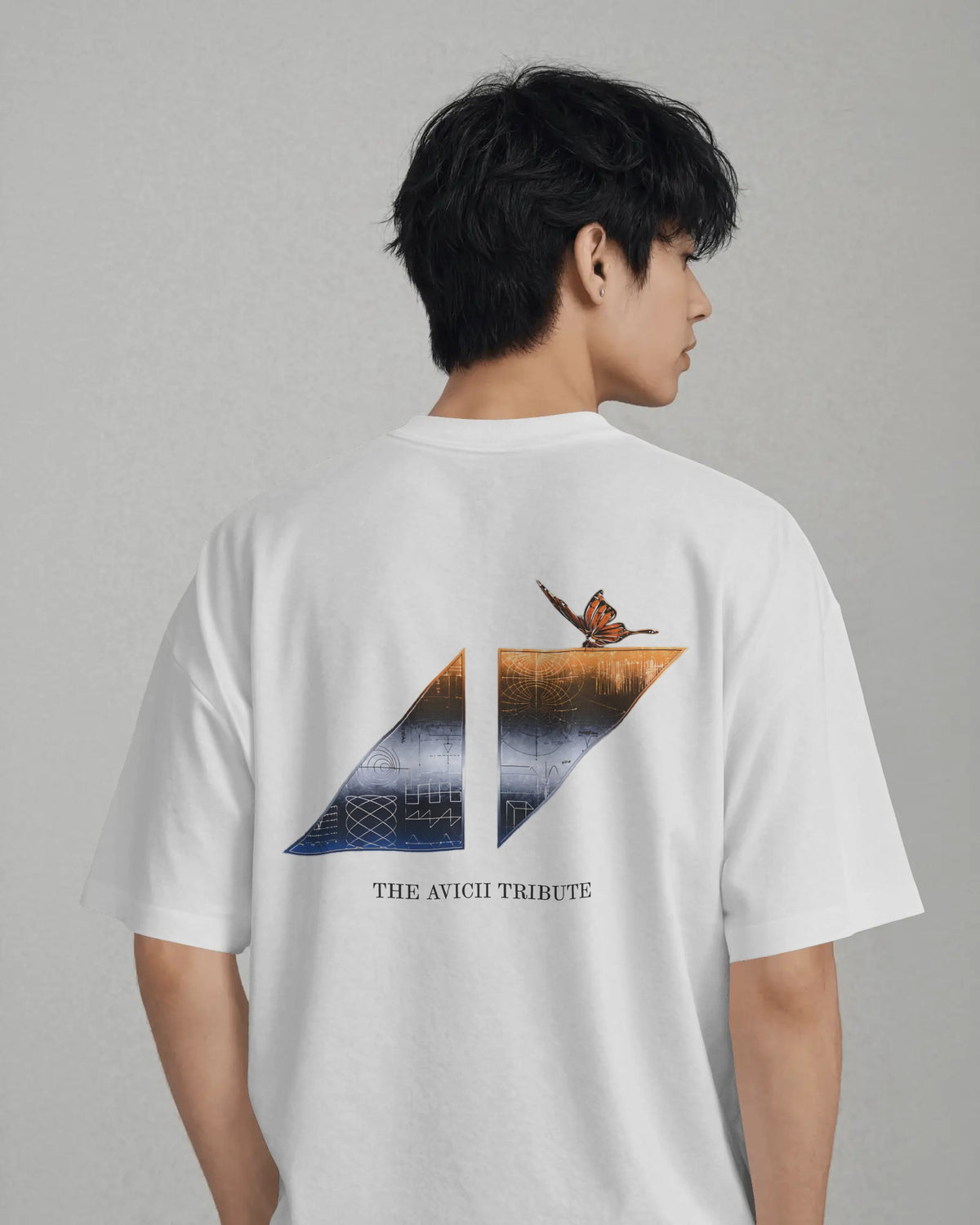 A man shown from the back wearing a white short-sleeve T-shirt with a large graphic print on the back. The graphic features a split geometric design in blue and orange-brown tones with a bird perched on the right side, and the text 'THE AVICII TRIBUTE' printed below.