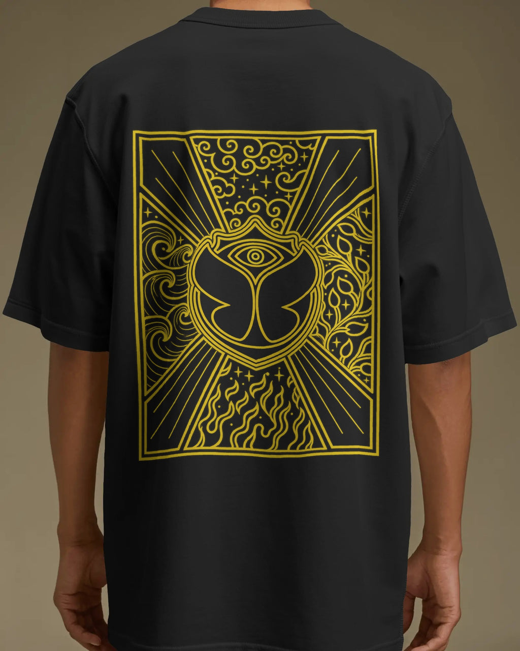 A person wearing a black short-sleeve T-shirt shown from the back, featuring a large yellow graphic print with an eye motif and ornate line art on the back. Nitorious Atelier Tomorrowland Concert collection