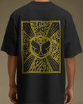 A person wearing a black short-sleeve T-shirt shown from the back, featuring a large yellow graphic print with an eye motif and ornate line art on the back. Nitorious Atelier Tomorrowland Concert collection