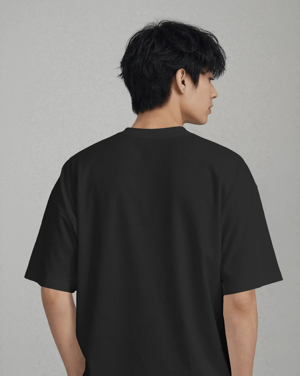 A man shown from the back wearing an oversized black short-sleeve t-shirt against a neutral gray background.