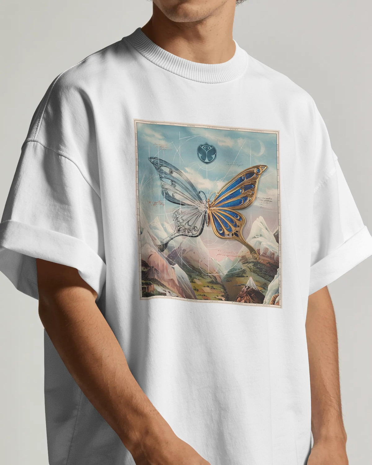 A person wearing an oversized white crewneck t-shirt with a large square graphic print on the chest depicting a surreal butterfly over a mountain landscape under a cloudy sky. Buy Tomorrowland Thailand Tshirt
