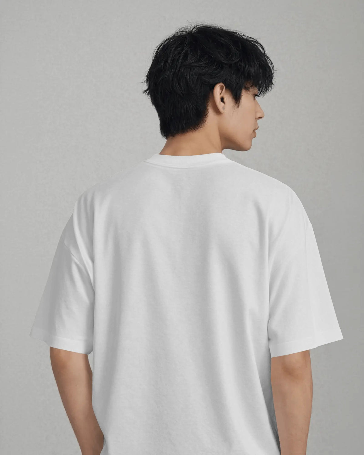 A man viewed from the back wearing an oversized white short-sleeve t-shirt against a neutral gray background.