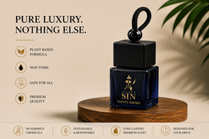 A dark blue glass car fragrance bottle with a black cap and loop, labeled 'SIN VELVET SMOKE', displayed on a wooden pedestal against a beige background with promotional text and a plant leaf. Silent Sin Automotive Elixir Car Fragrance from the house of Nitorious Atelier