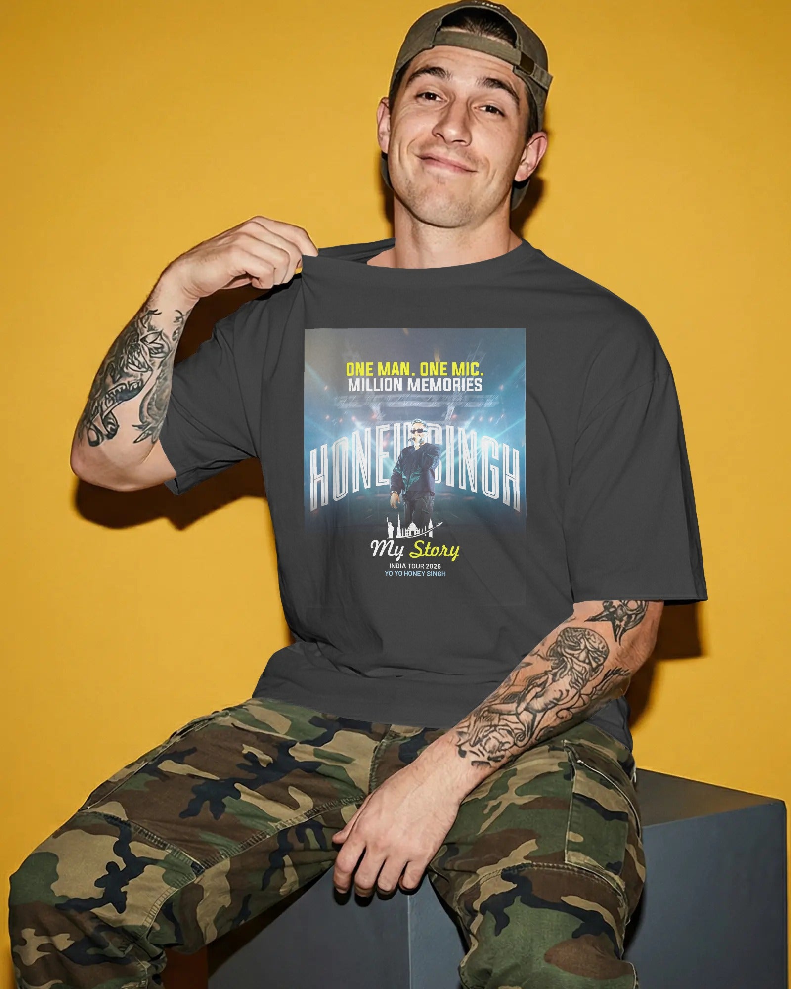 Man wearing a black t-shirt with graphic design and camouflage pants against a yellow background